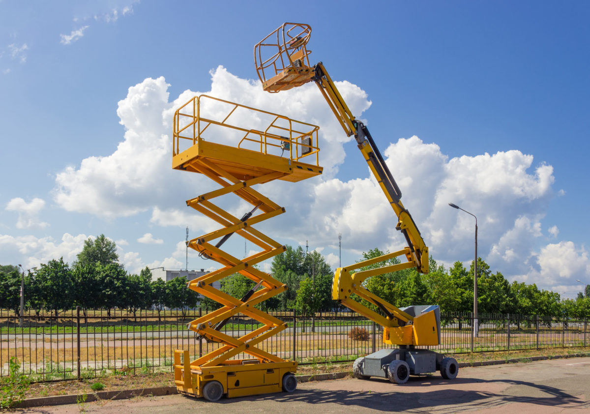 Yellow self propelled articulated boom lift and scissor lift on background of street with trees and sky